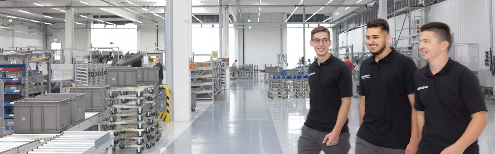 Drei Männer laufen in der Produktionshalle und lachen